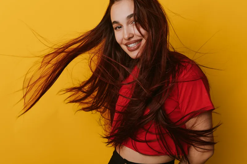 Young woman with long brown hair smiling and posing on yellow background. Casual style with red shirt and natural expression for lifestyle and happiness concept.
