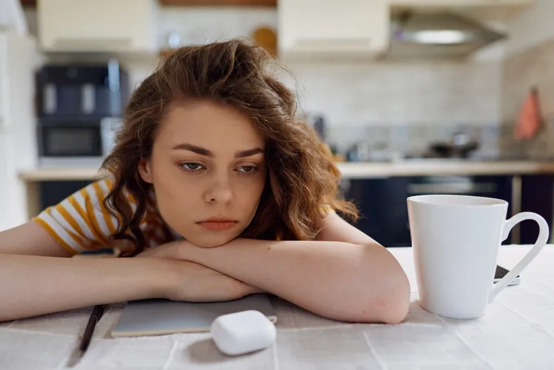 Calm woman indoors, resting chin on forearms, kitchen setting, muted colors, everyday moment, relaxed mood, natural light, domestic scene