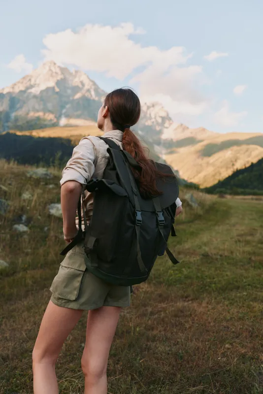 Young woman with a backpack hikes through a mountain valley enjoying the scenic view on a clear day with soft sunlight and natural surroundings.