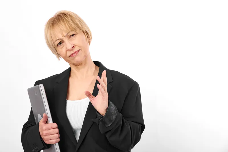 Older woman holds tablet, waves hand for greeting, business suit, conveys communication, confident face, isolated on white studio background