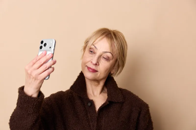 woman elderly smartphone selfie portrait closeup communication technology digital phone, eyes closed calm senior face, warm background concept of digital connection