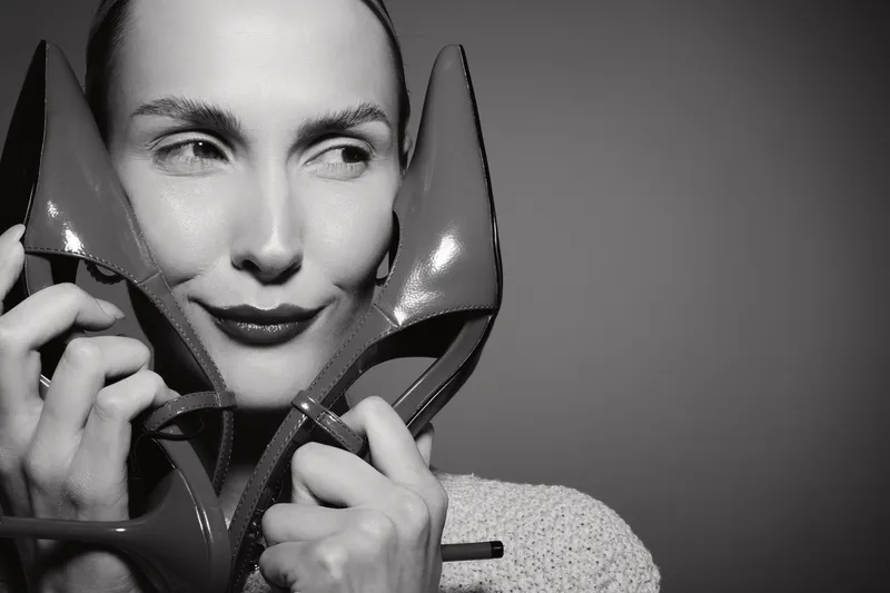 Close up of white woman with fair skin holding pair of high heel shoes near face in black and white photo.