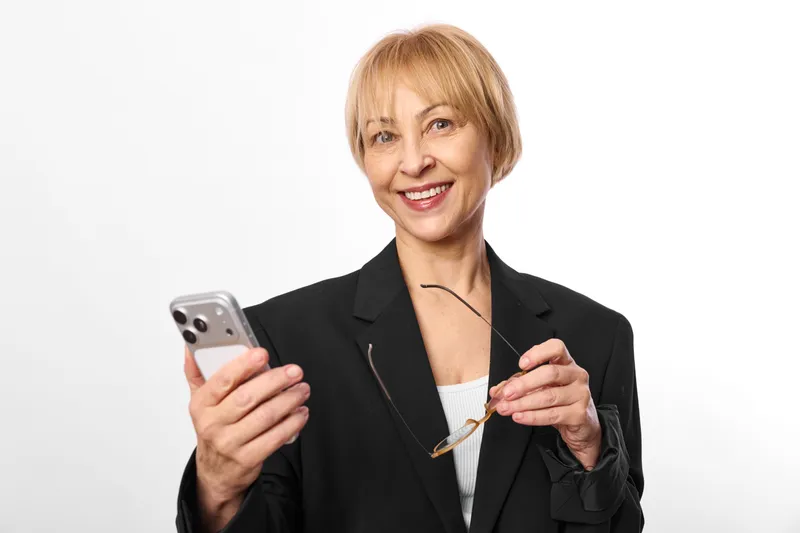 Senior woman business portrait in studio, holding smartphone with both hands, calm smile, technology communication and online digital concept on neutral background