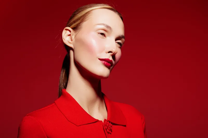 Elegant woman with slicked back hair and red lipstick poses against red background wearing a red collared top. Concept of fashion, beauty, style, and confident female portrait.