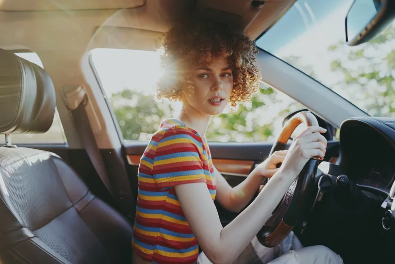 Woman driving in a sunny car, outdoors, striped colorful shirt, candid moment, relaxed posture, carefree lifestyle with a retro feel and vivid film color