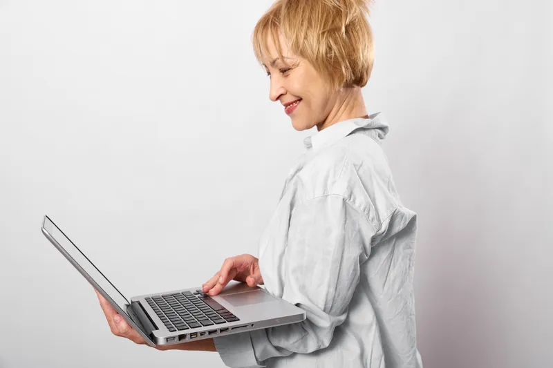 Woman using laptop for typing in profile, technology and communication for work, smiling in studio, clean neutral background, soft light