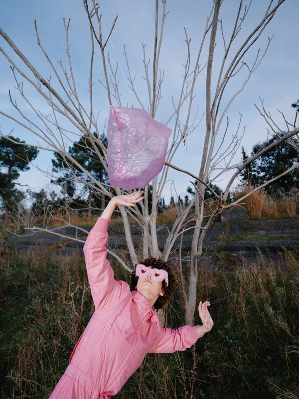 Pink dress girl releasing a lantern outdoors among trees, a festive moment as the wind lifts the lantern toward the sky under a clear blue evening.