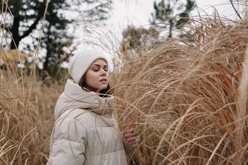 Winter portrait, outdoors, grass, nature, woman, coat, calm, thoughtful, field setting with tall dry grasses and soft neutral tones, cozy outerwear and serene mood in a chilly daytime scene