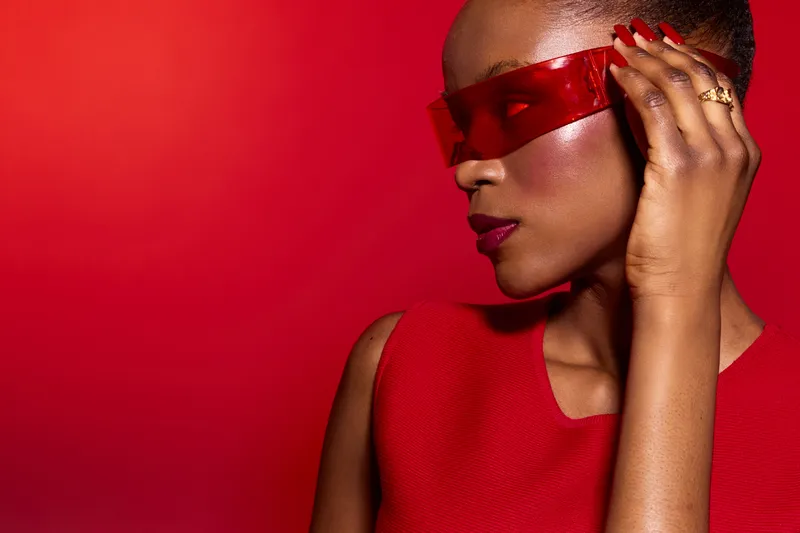 Portrait of a dark skinned African woman wearing red futuristic sunglasses and red sleeveless dress against red background. Concept of fashion, style, beauty, and modern accessories.