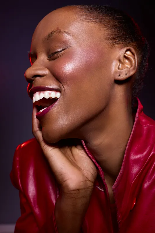 Portrait of happy dark skinned African American woman with closed eyes laughing, wearing red leather jacket. Concept of joy, beauty, fashion, and positive emotion in studio lighting.