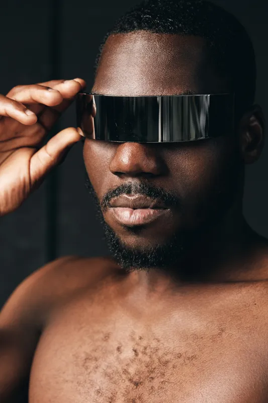 Creative conceptual portrait of African man wearing futuristic reflective visor in visual style. Closeup of dark skin male with modern accessory for innovative fashion and technology.