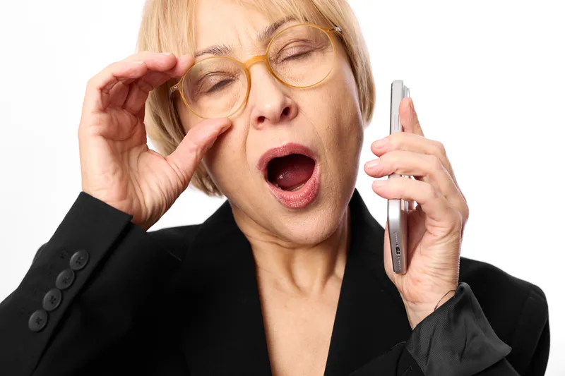 Business portrait of a woman with glasses adjusting frames while holding smartphone to ear, surprise expression, open mouth, studio background, communication concept