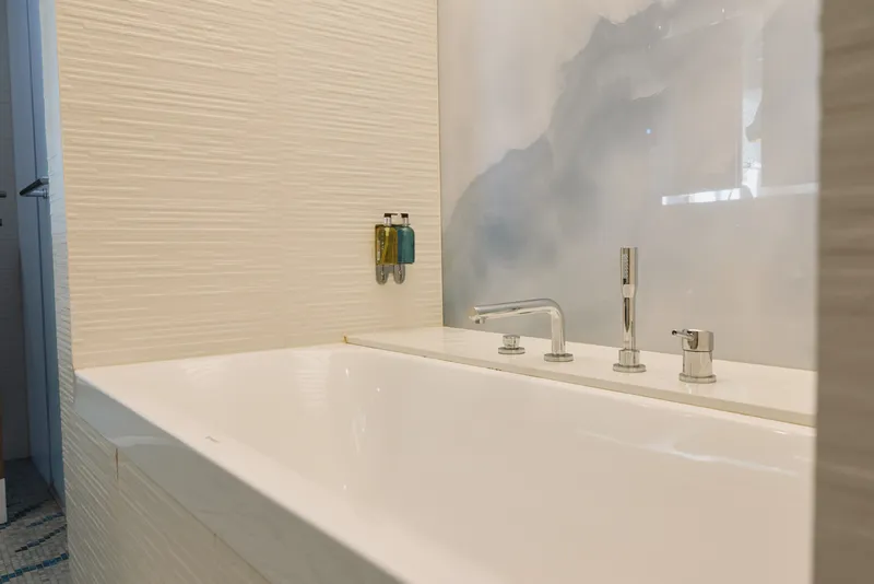 Modern bathroom with white bathtub and sleek faucet, tiled walls and a large glass window creating a bright, serene spa atmosphere.