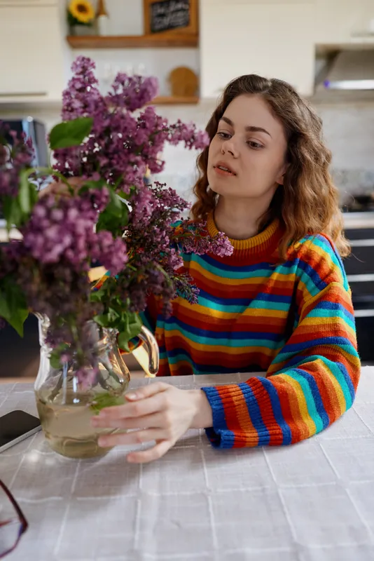 A woman in a striped sweater sits at a kitchen table, arranging a bouquet in a vase, creating a cozy home moment in a bright indoor lifestyle setting that feels calm and welcoming.