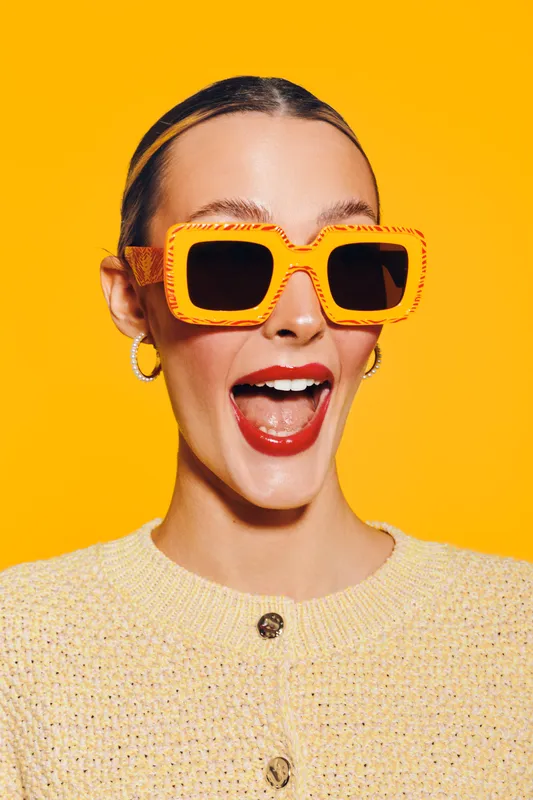 Happy woman with bright orange sunglasses and red lipstick smiles widely on yellow background. Fashion portrait with vibrant colors and joyful expression. Concept of style and fun.