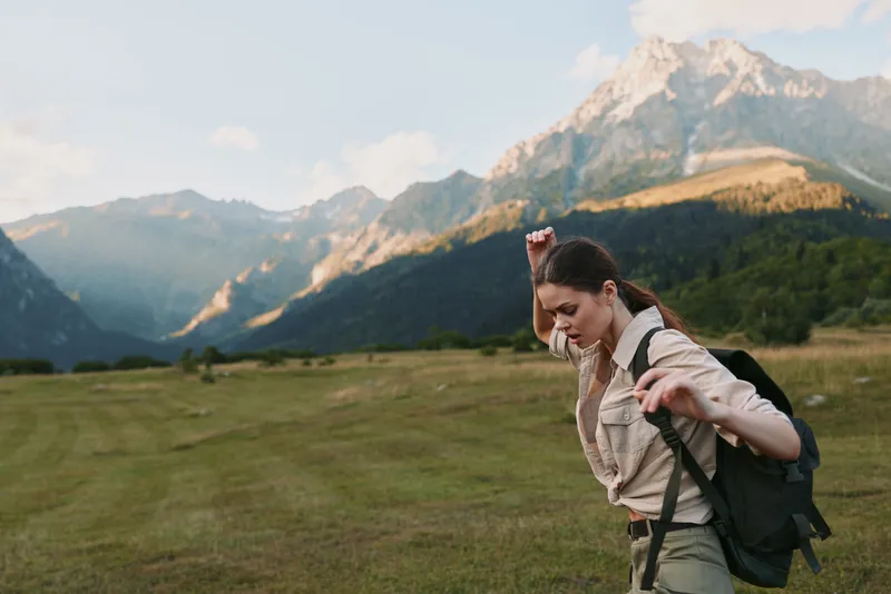 Active woman hiking in a mountain valley with a backpack, sunlight on the landscape, outdoors, travel, fitness, nature, adventure, and exploration in a bright, fresh scene.