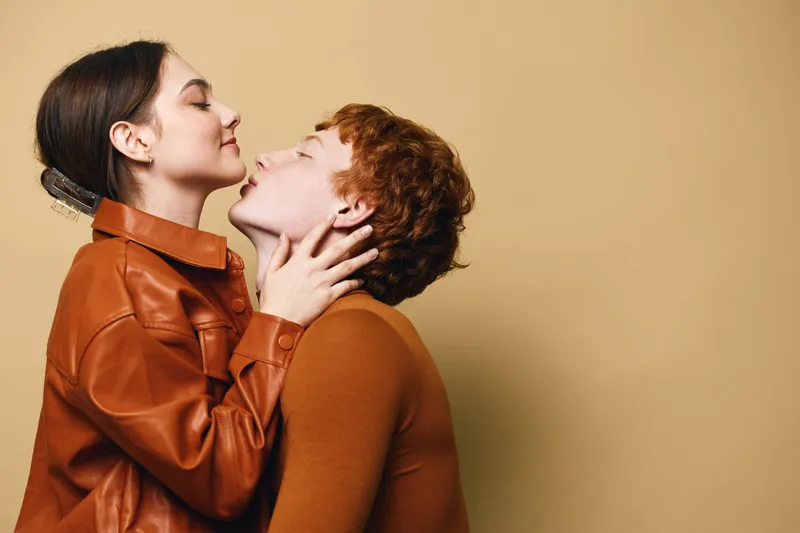 Couple in love embracing indoors with warm clothing, woman gently holding man’s face, close romantic moment against plain background for relationship and affection.
