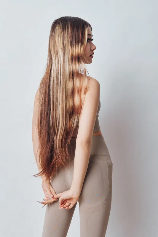 Woman with long straight hair and casual outfit standing side view with hands behind back on light background for beauty and fashion portrait.
