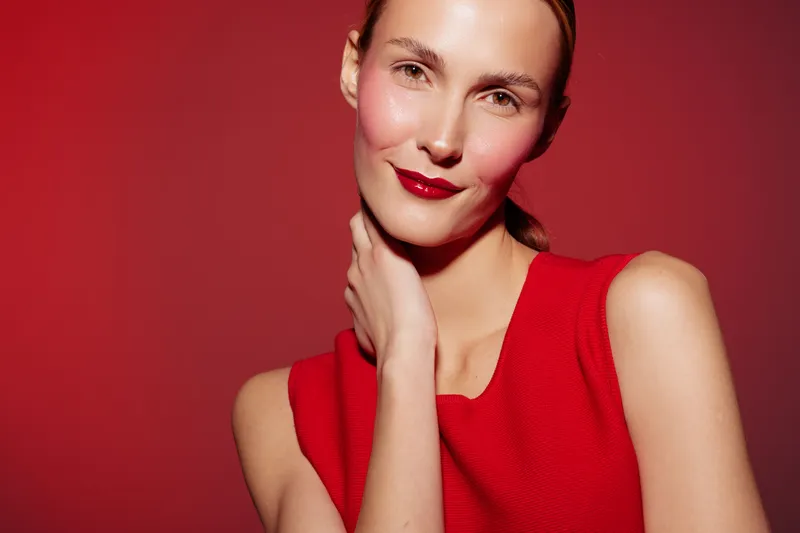 Portrait of a smiling woman in red dress with natural makeup and red lipstick on red background. Concept of beauty, fashion, confidence, and elegance in studio lighting.