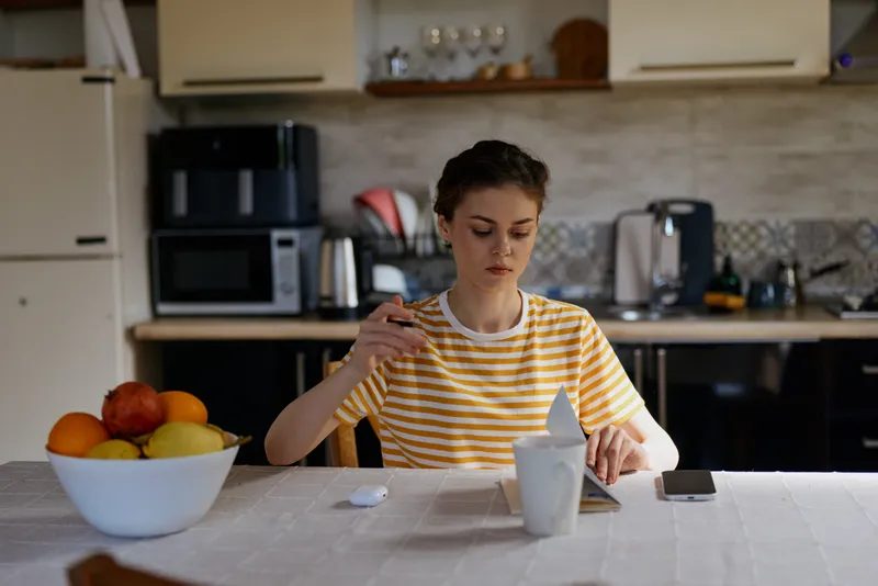 One person, young woman, brunette, striped tshirt, kitchen, casual, focused, pouring into mug while glancing at phone, calm morning mood, home life, quiet