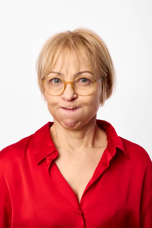 Senior woman portrait, short blonde hair, round glasses, red shirt, calm expression, looking at camera, studio background, healthcare age concept, friendly smile