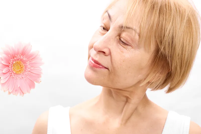 Woman, pink, flower, closeup, profile, eyes, closed, aromatherapy, calm, wellness, gentle smile, smelling fragrance, relaxed facial expression, soft studio lighting on white background, spring blossom
