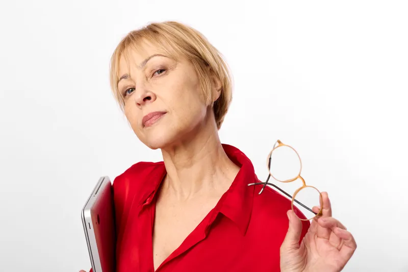 Elderly woman holds glasses and eyeglasses while checking the lens frame, concerned about vision and eyesight during optometry consultation, studio portrait