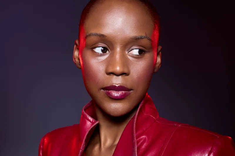 Portrait of a dark skinned African woman wearing a red leather jacket looking sideways on a dark background. Concept of fashion, beauty, confidence, and strong personality.
