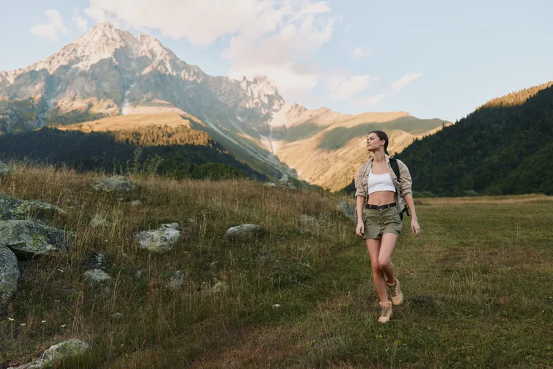 Young woman hiking in the mountains wearing shorts and a backpack. Outdoor lifestyle concept with natural landscape and sunny weather. Adventure and freedom.