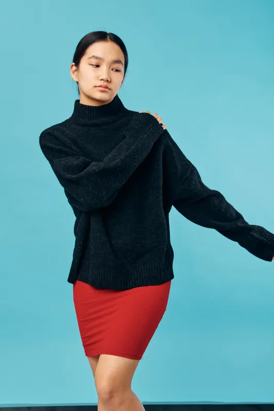 Young woman wearing black sweater and red skirt posing against blue background for fashion portrait, casual clothing, lifestyle, and style concept with confident expression.