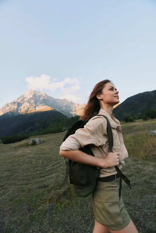 Young woman hiking in the mountains with a backpack, enjoying nature and fresh air. Outdoor lifestyle, adventure, and freedom in a scenic landscape with clear sky.