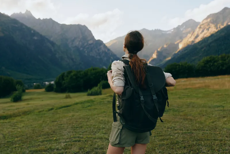 Young woman with backpack hiking in mountain valley, exploring nature, casual outfit, scenic landscape, outdoor adventure, summer day, active lifestyle