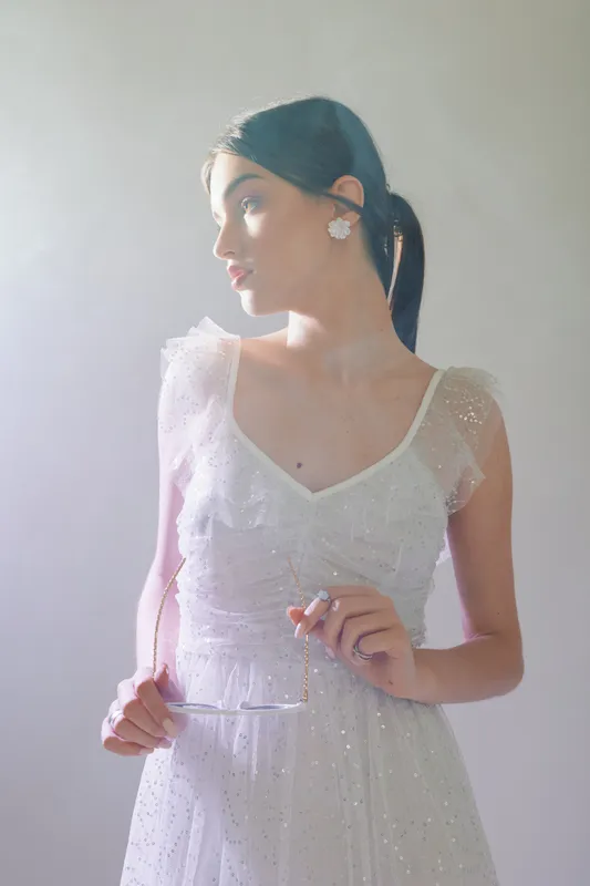Young woman in elegant white dress poses holding glasses. Soft natural light highlights her beauty and fashion style. Concept for beauty, fashion, and elegance.
