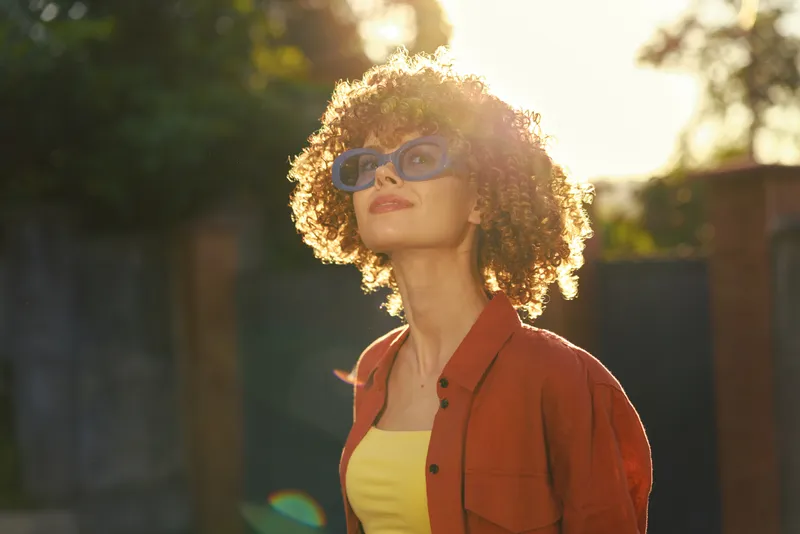 Woman lifestyle outdoors, cheerful portrait of a curly haired woman in a sunlit moment, wearing a red shirt and yellow top, relaxed and stylish