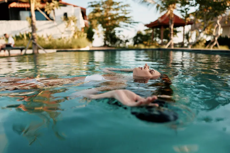 A person floats in a clear pool with outstretched arms relaxed mood in a sunny outdoor setting tranquil water and leisure lifestyle vibe focused on personal relaxation