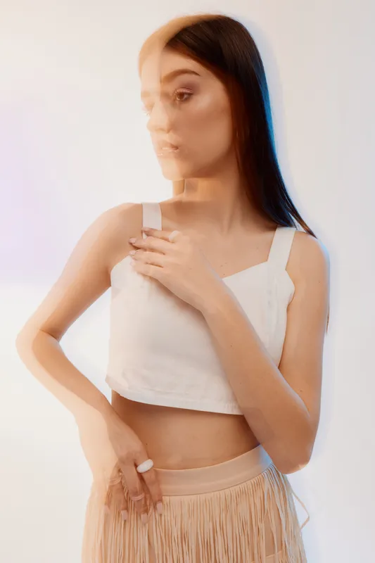 Young woman in a white top and beige skirt poses with hand on chest. Soft lighting and blurred effect create a dreamy beauty and fashion concept.