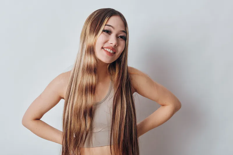 Young woman with long braided hair wearing a sleeveless top smiling and posing against a plain white background indoors. Beauty confident happy gesture casual style.