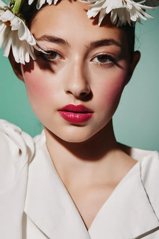 Close-up portrait of a young woman with creative floral makeup and bold red lipstick looking into the camera. Concept of beauty, fashion, colorful style, makeup artistry.