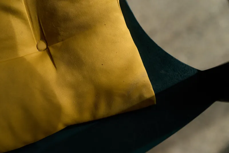 Close-up of color-block fabric in mustard yellow and dark green with a subtle textile texture and a small button, emphasizing material detail, color contrast and tactile quality.