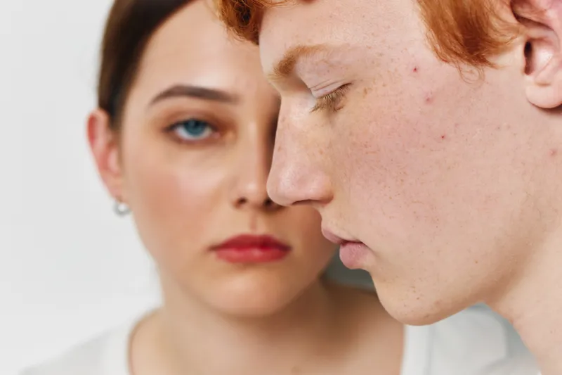 Closeup portrait of young man and woman with serious expressions on white background. Focus on natural skin details and emotional mood between two people.