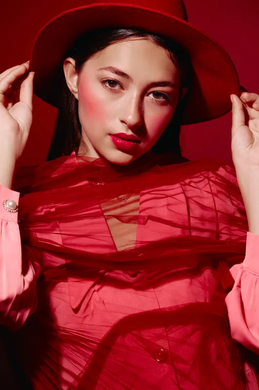 Young woman in a red hat and vibrant red dress with artistic makeup poses with intense expression. Concept for beauty, creative fashion photography.