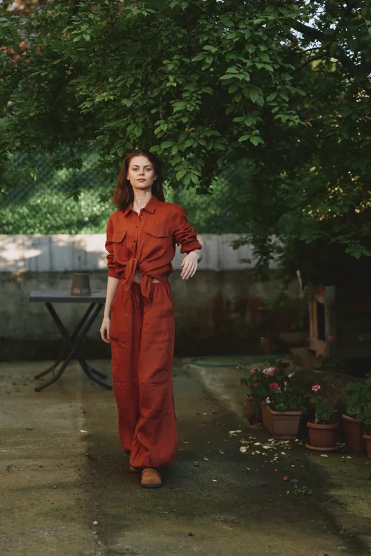 A woman in a red jumpsuit walks through a garden setting, relaxed yet confident. A lifestyle portrait capturing contemporary fashion and natural light