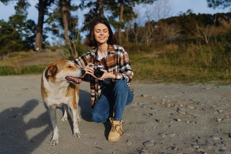 woman dog outdoors camera kneeling beach nature portrait photography moment friendship relaxed sunlight gravel shore girl outdoor scene candid adventure