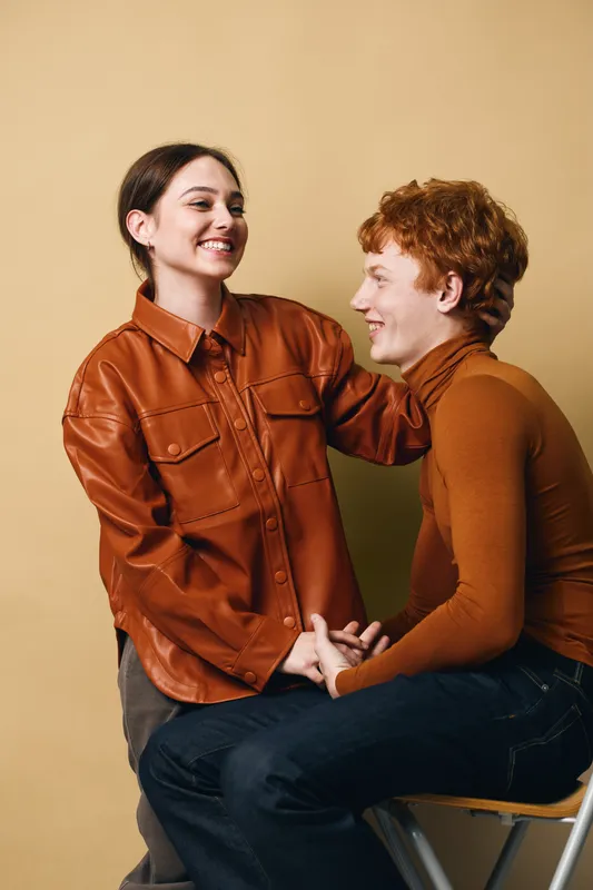 Young couple smiling and holding hands dressed in autumn fashion with brown tones against beige background. Love, connection and friendship between two people in studio.