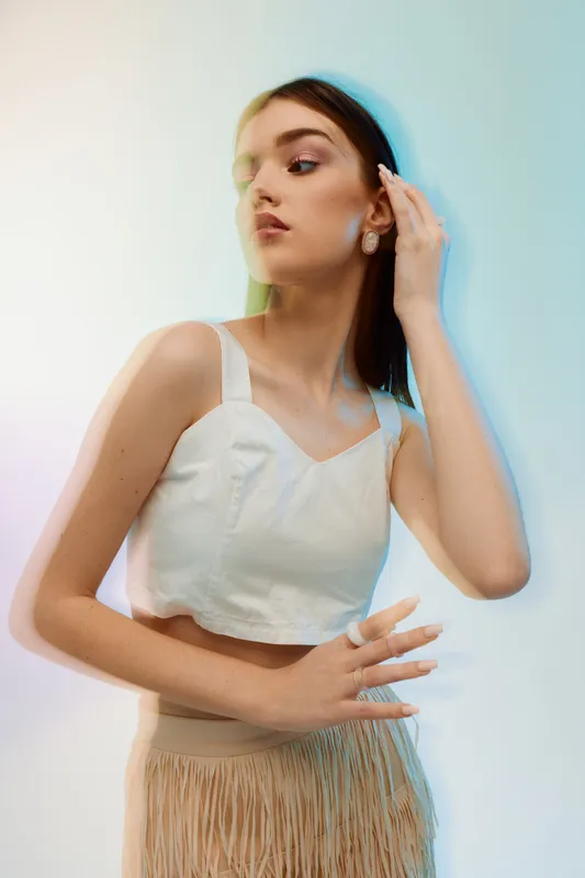 Young woman in a white top and beige skirt poses gracefully against a light background. Concept of beauty, fashion, elegance, and modern style with soft lighting.