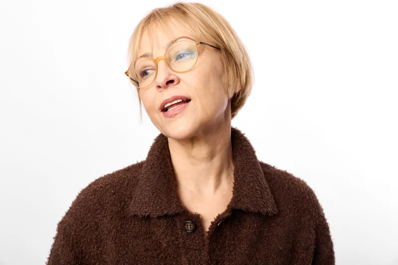 Senior woman with glasses in a studio portrait, closeup face and mouth open, surprised expression with a hint of worry, clean white background, calm indoor lighting