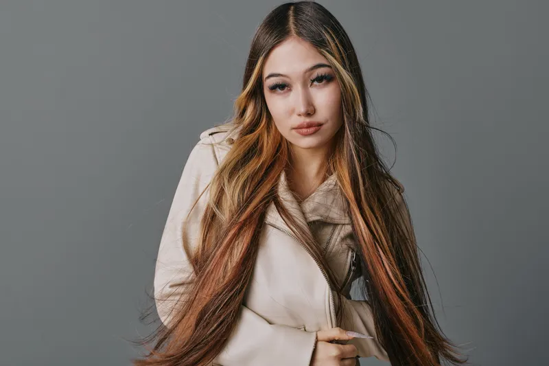 Young woman with long hair wearing a light coat posing on gray background for fashion portrait and casual style in studio with serious expression and natural makeup.