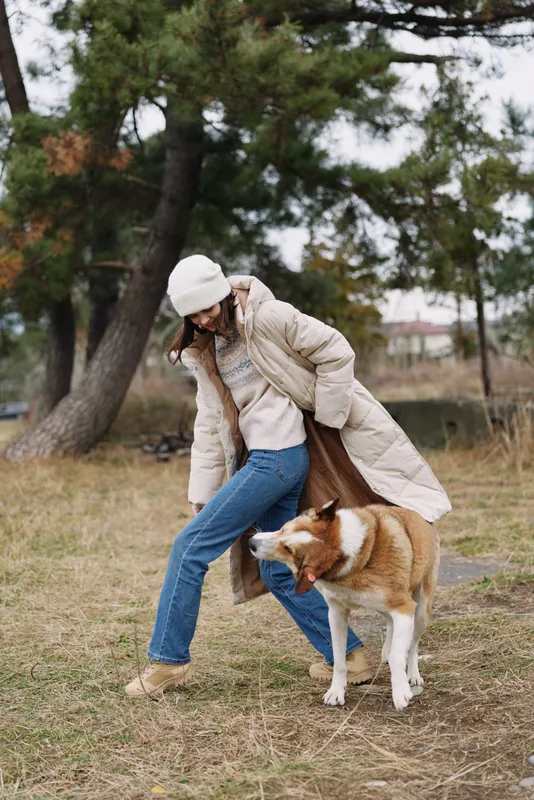 woman, dog, walking, park, coat, autumn, outdoor, companionship, casual, lifestyle, Woman in a warm coat and beanie walks a dog in a park, autumn light, casual outdoor leisure, candid moment of