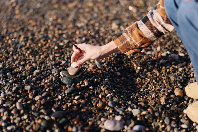 Closeup of a hand in a plaid sleeve pressing a smooth pebble on a rocky beach, capturing texture, focus and casual outdoor exploration during a sunny day by the sea.
