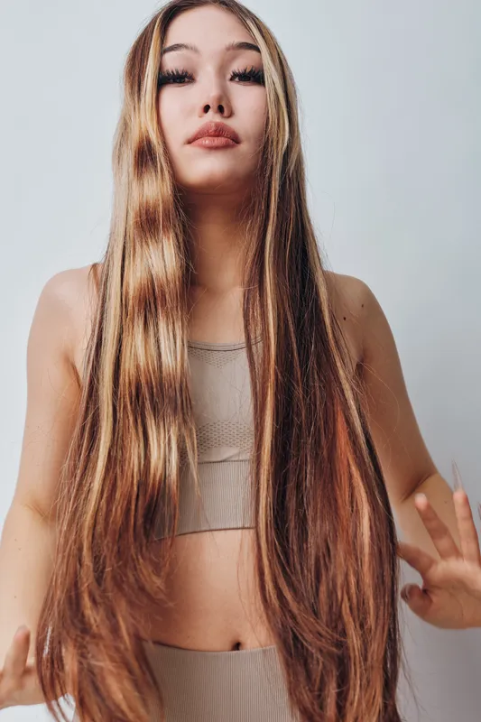 Young woman with very long straight hair posing against plain background wearing neutral color top and bottom awaiting expression and style for fashion or beauty concept.